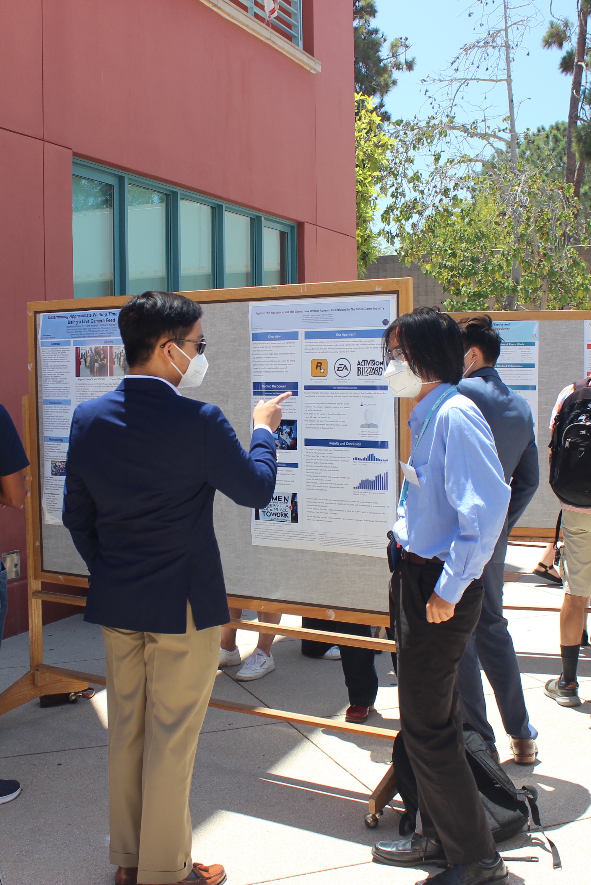 a man pointing at the poster of an SRA student who is explaining the project