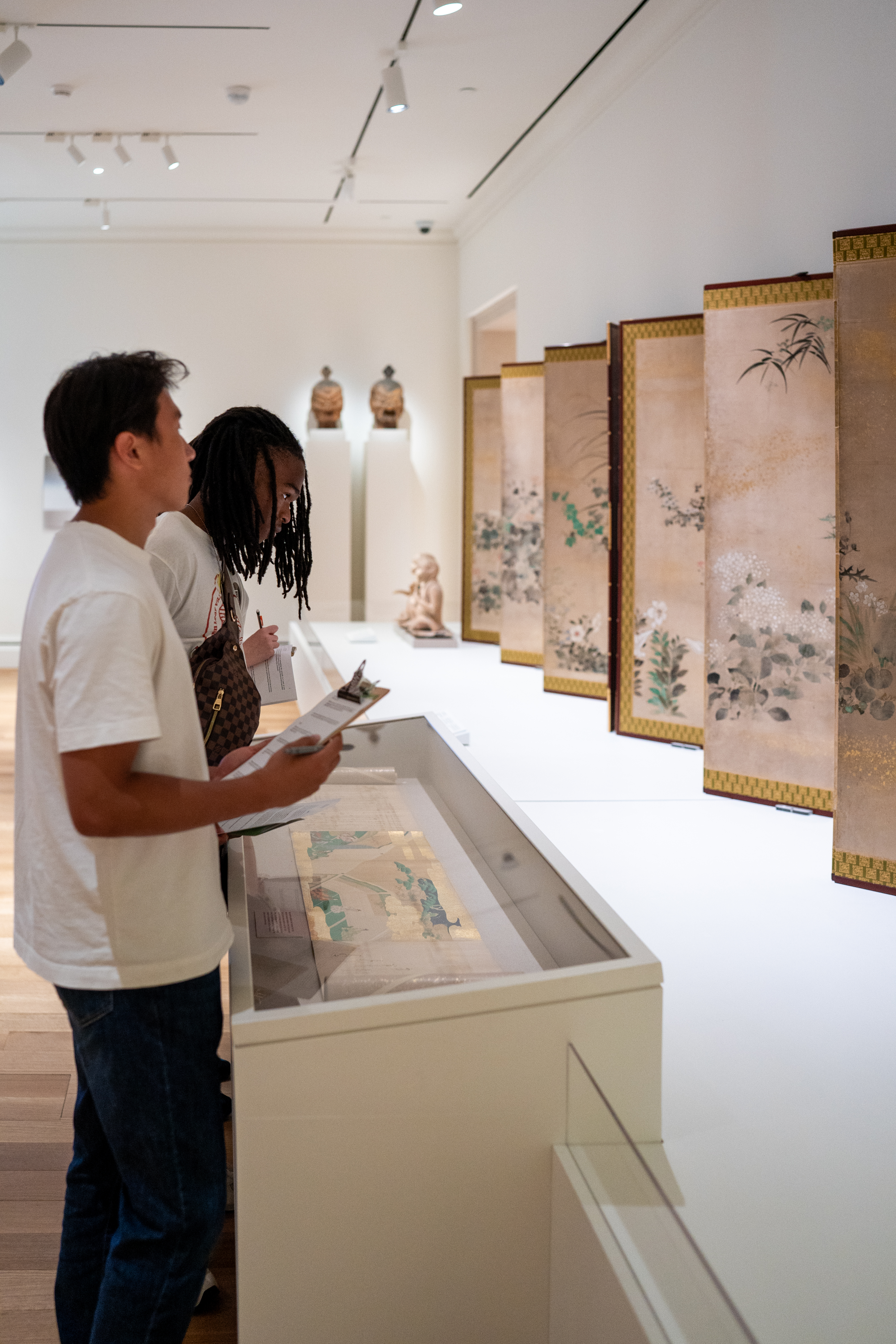 two SRA students examining art and taking notes in a museum