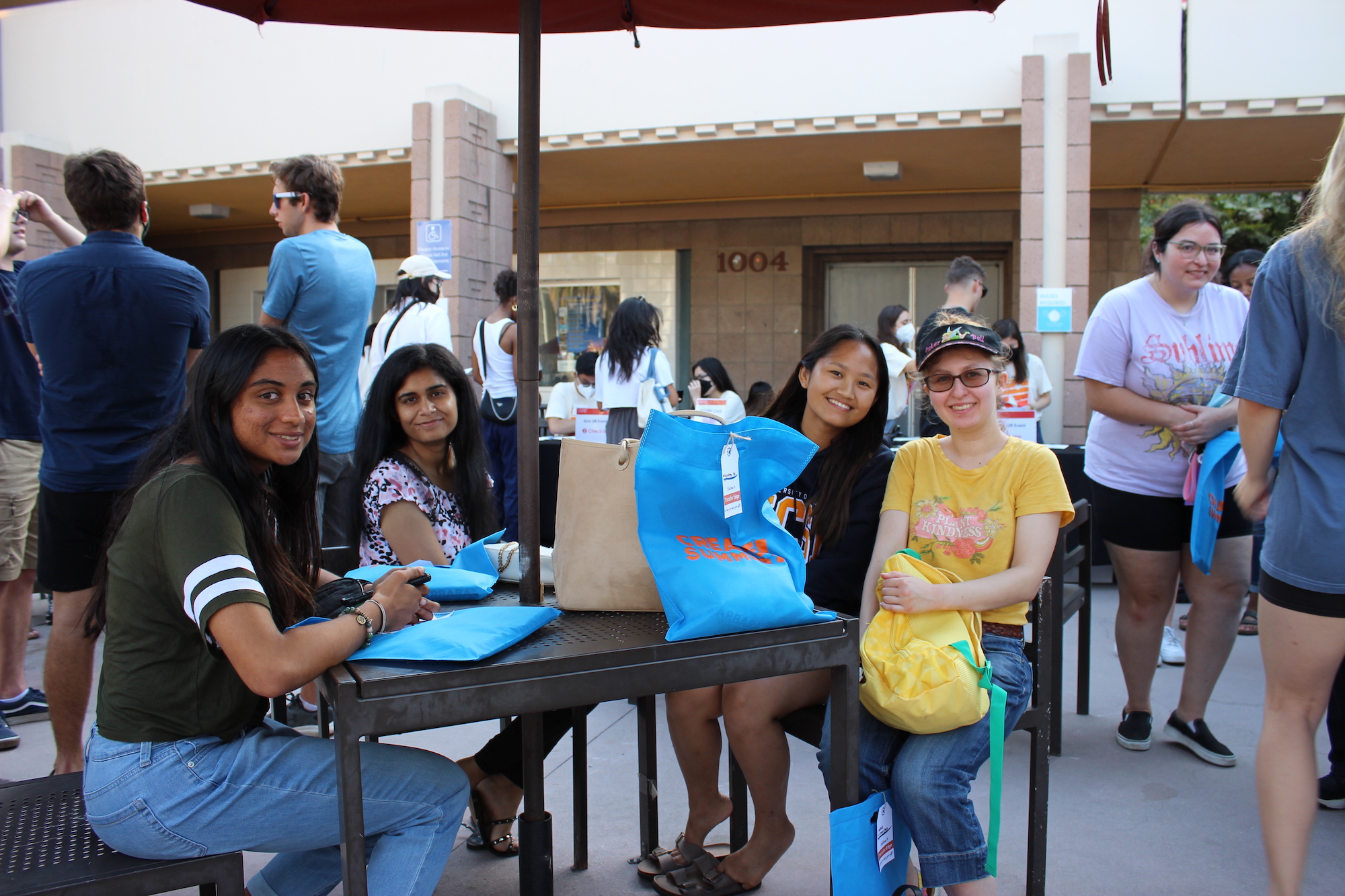 four students smiling and sitting at a table outside