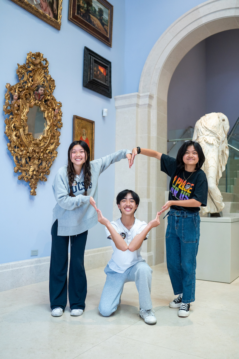 three SRA students in a museum making a heart with their arms