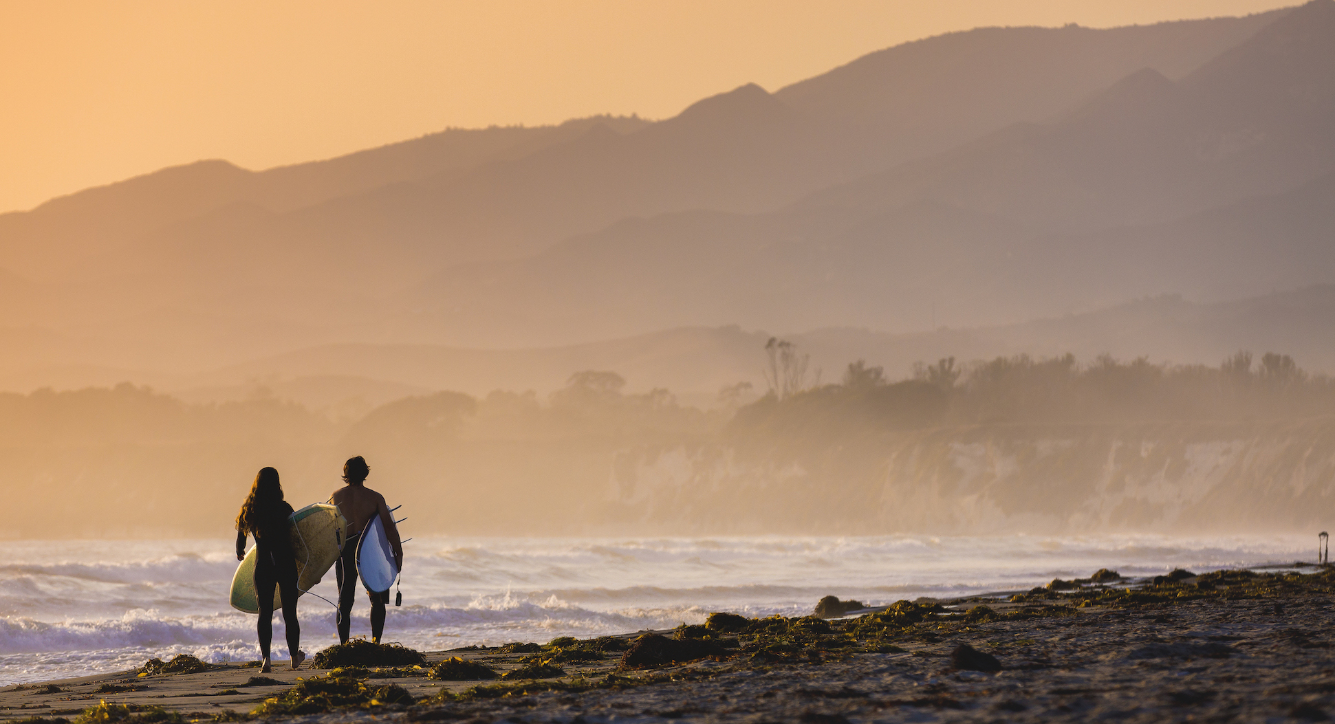 two surfers walk on coast at dusk