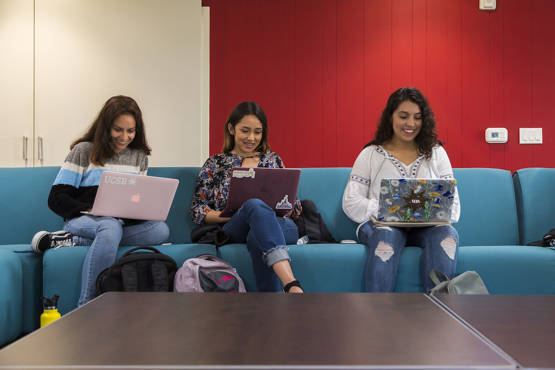three students sitting on a couch on their laptops